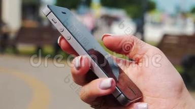 年轻漂亮的女人在公园的手机上拨一条短信。 女子手拨电话短信的特写